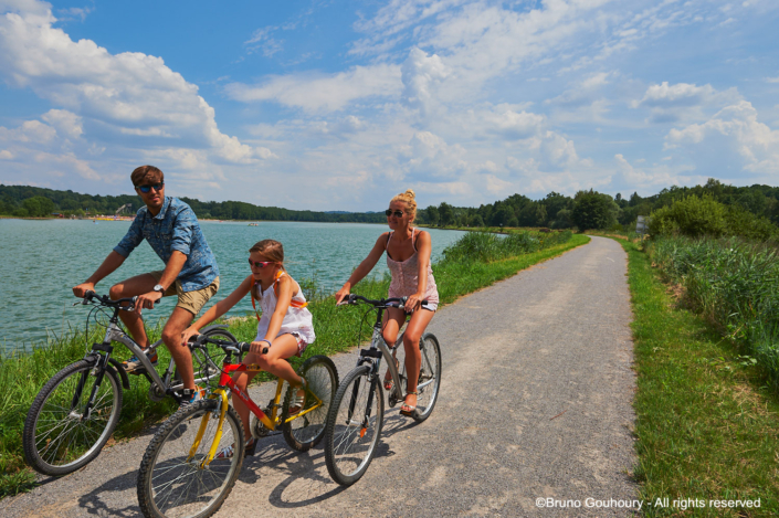 velo tourisme mobilite piste cyclable riviere Famille à vélo sur une piste cyclable le long d'un cours d'eau